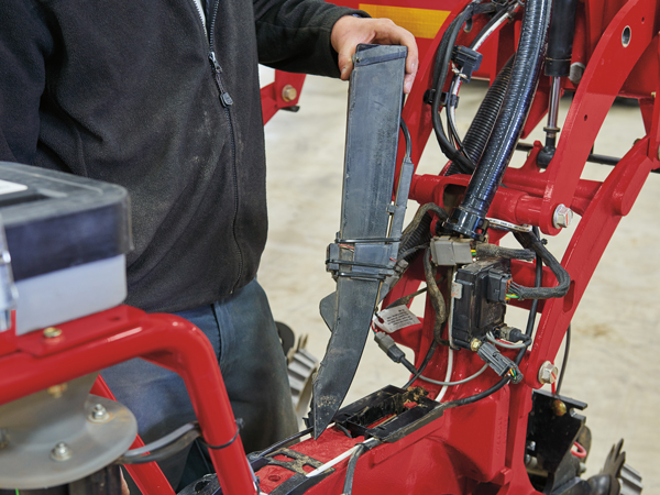 A person standing by a red machine and holding a component attached to the machine.